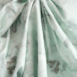 Crumpled fabric yardage in a dense photorealistic floral print in shades of gray and pastel green.