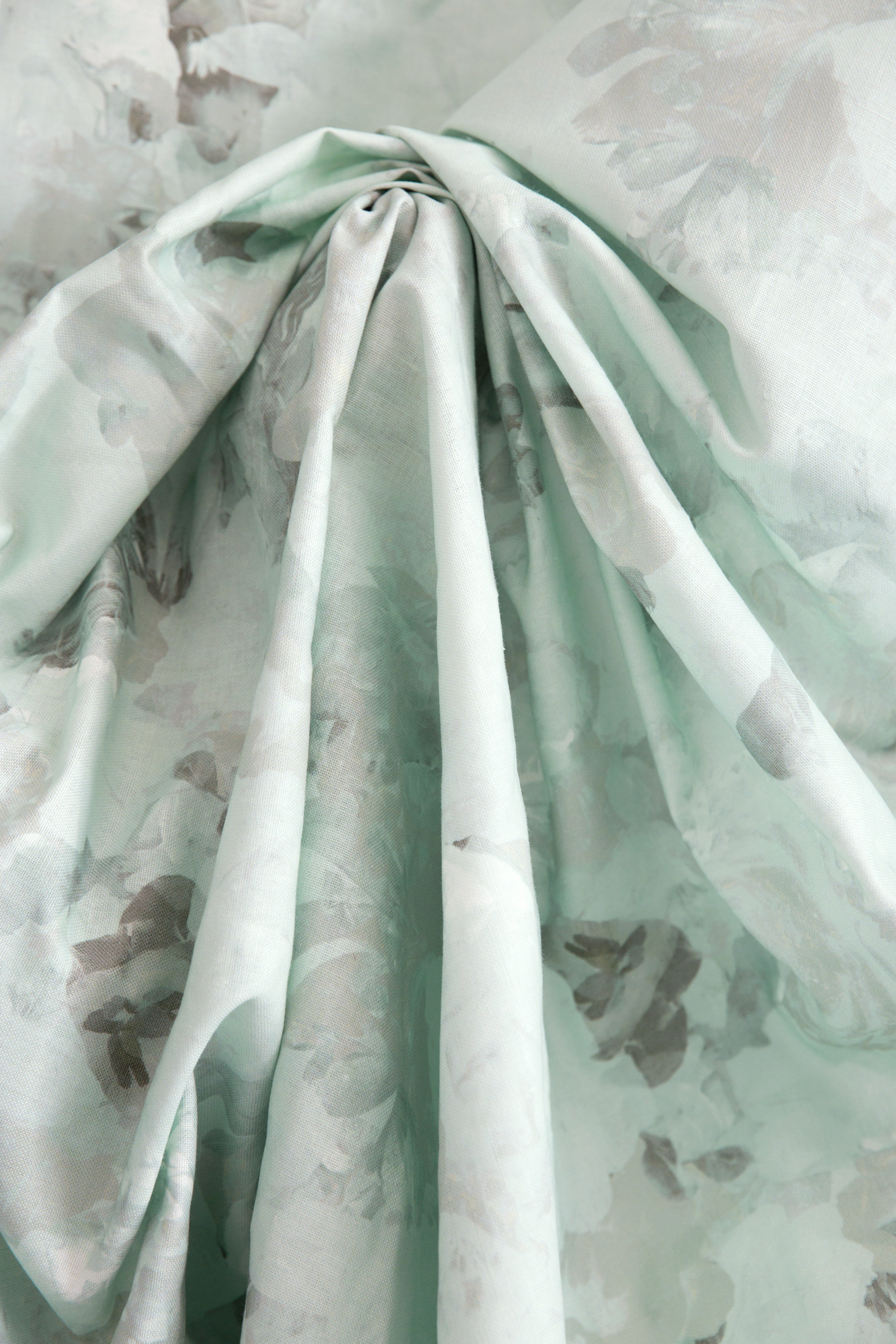 Crumpled fabric yardage in a dense photorealistic floral print in shades of gray and pastel green.