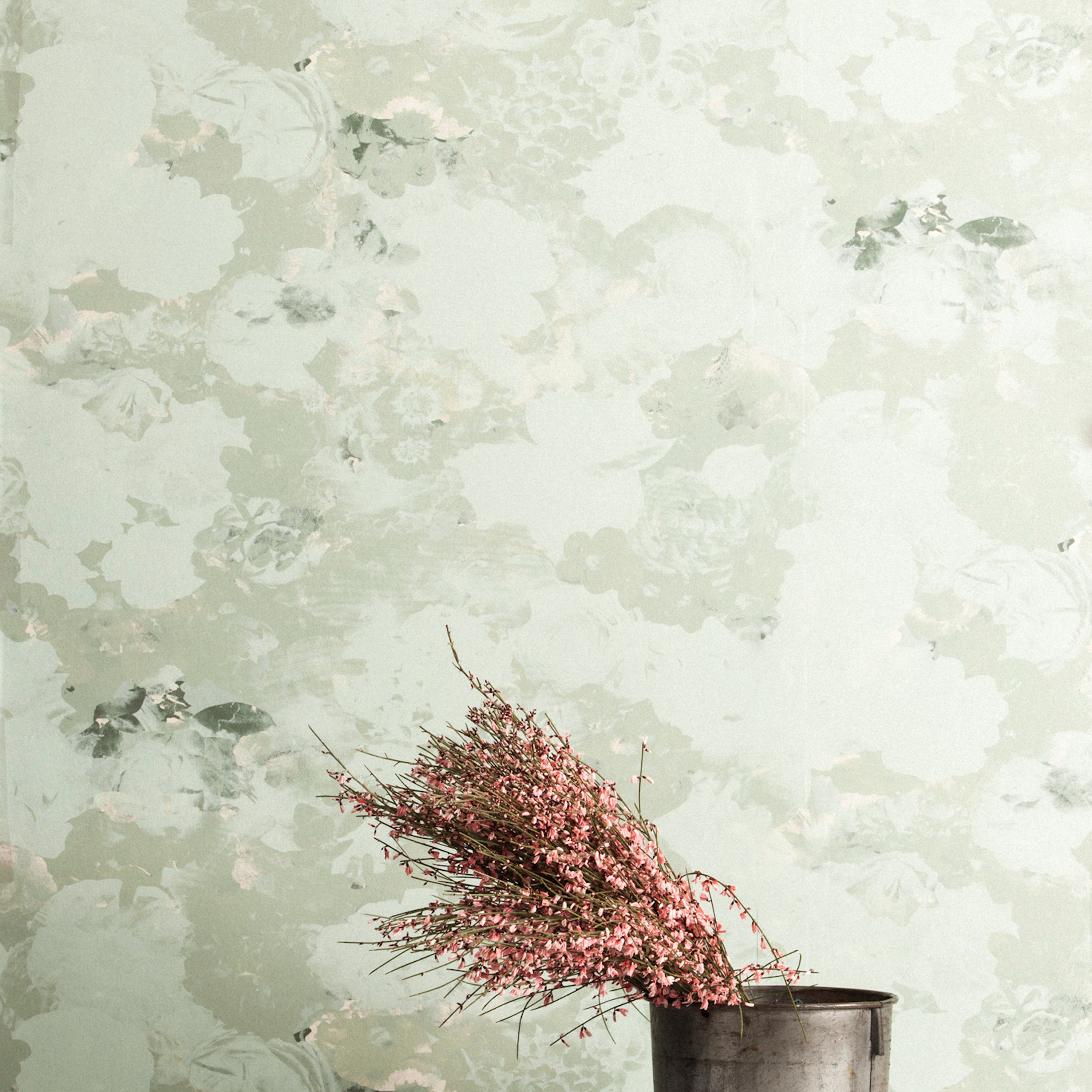 A vase of flowers stands in front of a wall covered in a dense photorealistic floral print in gray and pastel green.