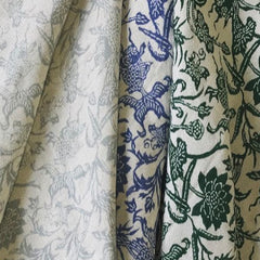 Draped pieces of three fabrics in gray, green and blue paisley floral prints on cream backgrounds.