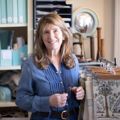 A woman with wavy brown hair and wearing a blue pleated button-down stands next to a rack with swatches of interior fabrics.