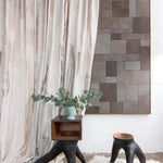 Modernist end tables stand in front of a curtain in an abstract paint print in shades of pink, brown and gray on a cream field.