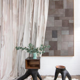 Modernist end tables stand in front of a curtain in an abstract paint print in shades of pink, brown and gray on a cream field.