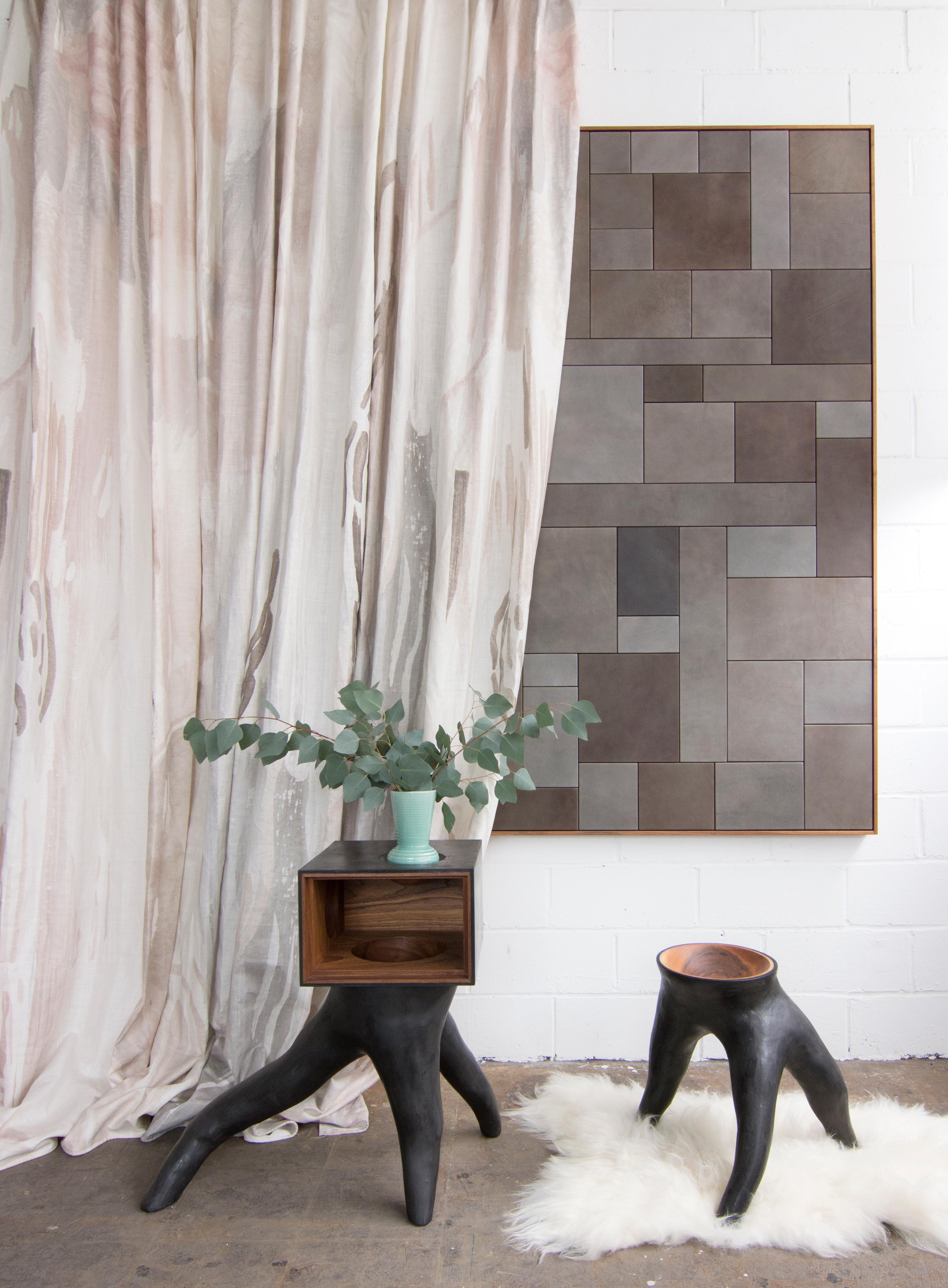 Modernist end tables stand in front of a curtain in an abstract paint print in shades of pink, brown and gray on a cream field.