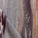 Draped fabric yardage in an abstract paint print in shades of gray, orange and purple on a cream field.