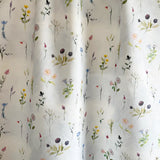 Draped fabric yardage in a painterly flower print in green and pastels on a cream field.