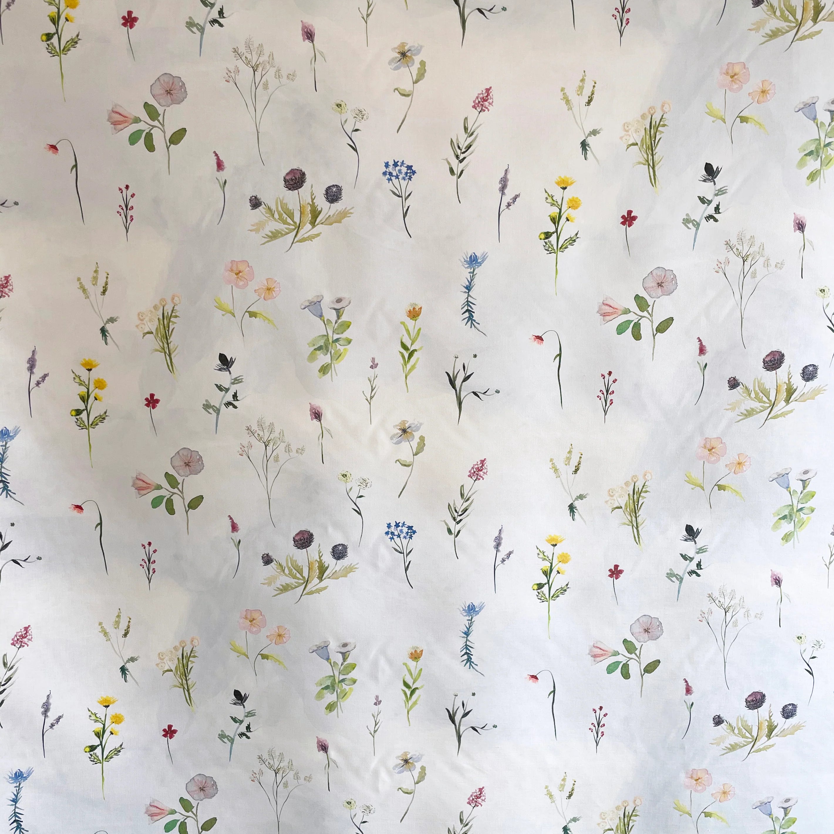 Draped fabric yardage in a painterly flower print in green and pastels on a cream field.