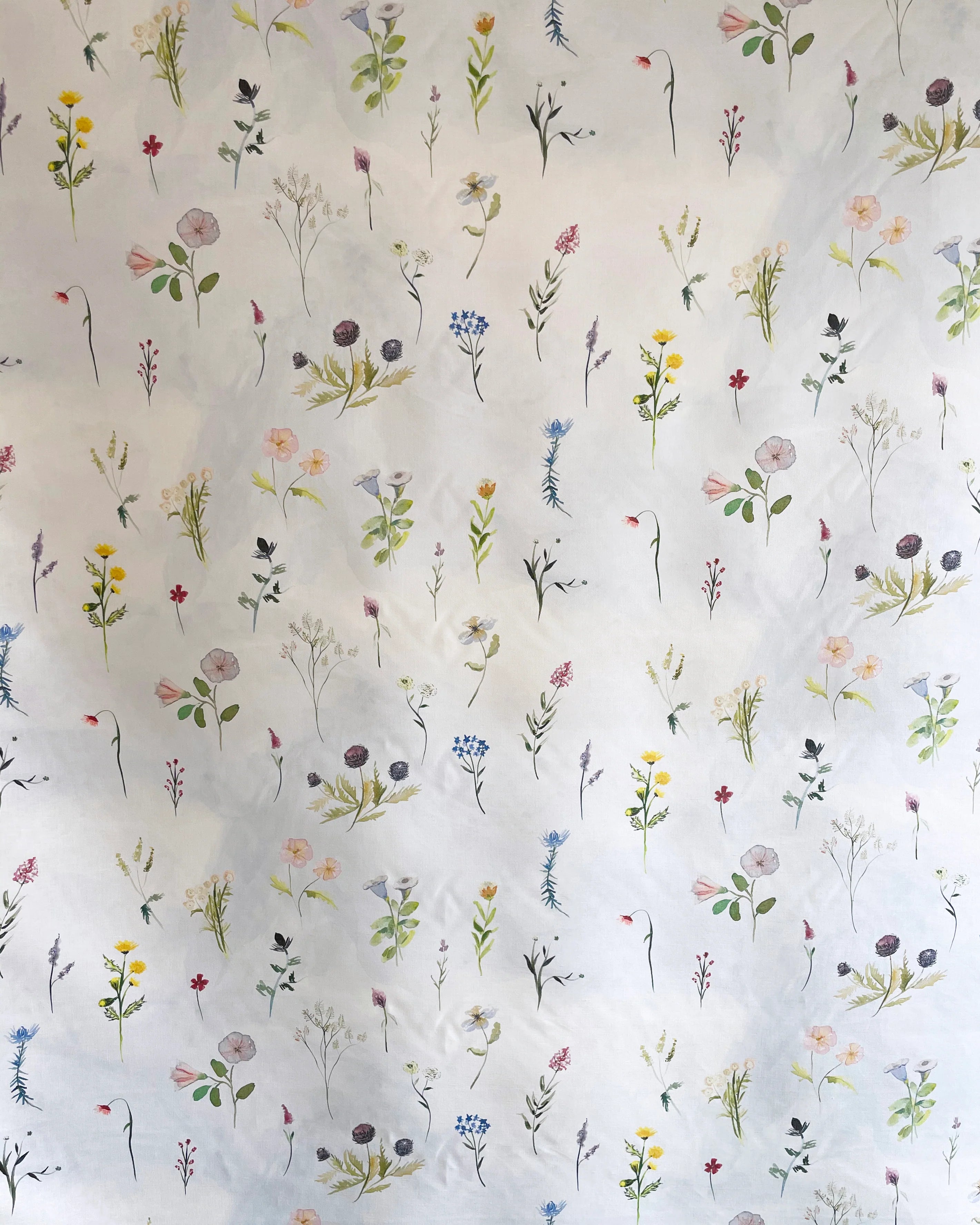 Draped fabric yardage in a painterly flower print in green and pastels on a cream field.