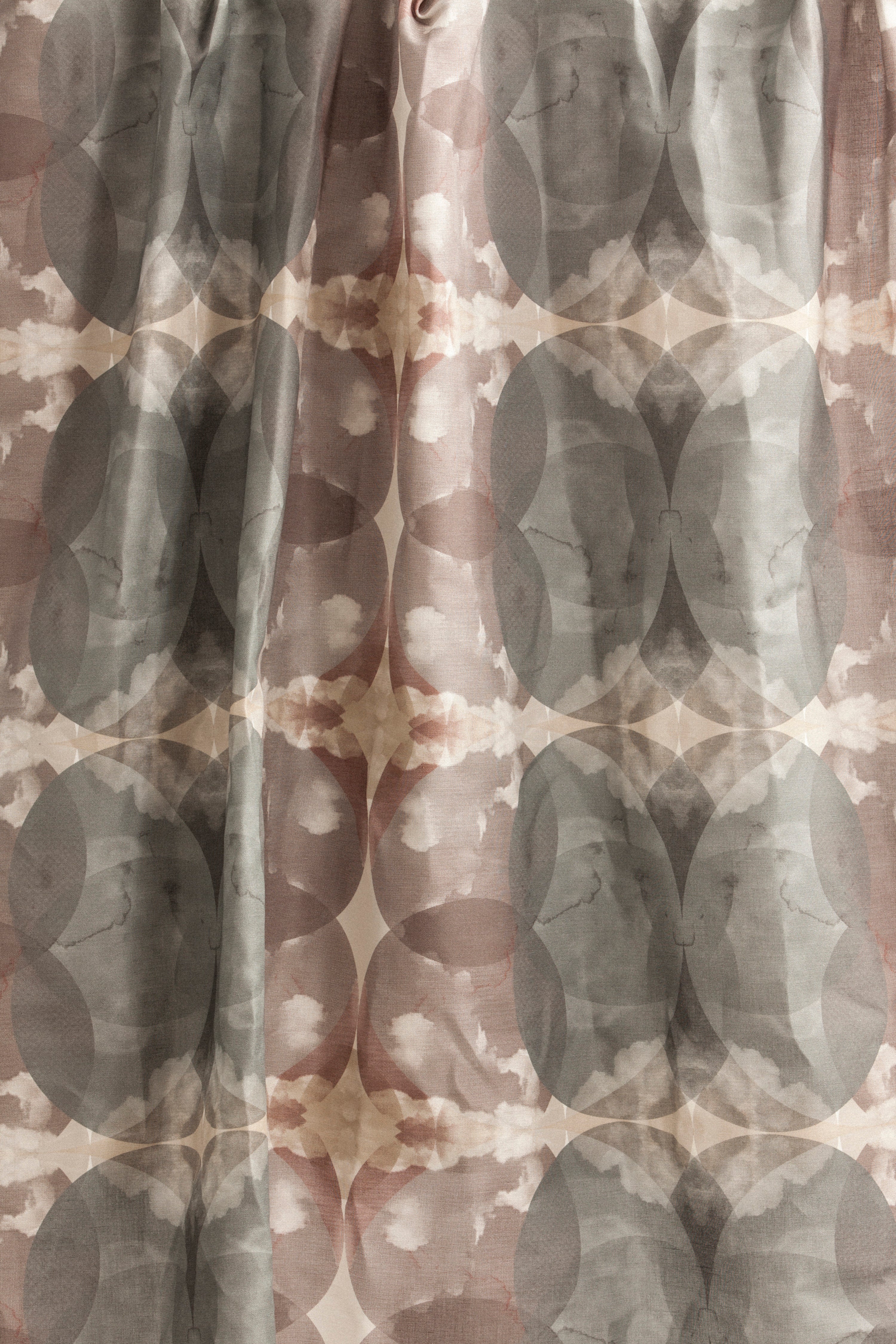 Draped fabric yardage in a cloudy ink blot print in shades of gray and pink on a cream field.