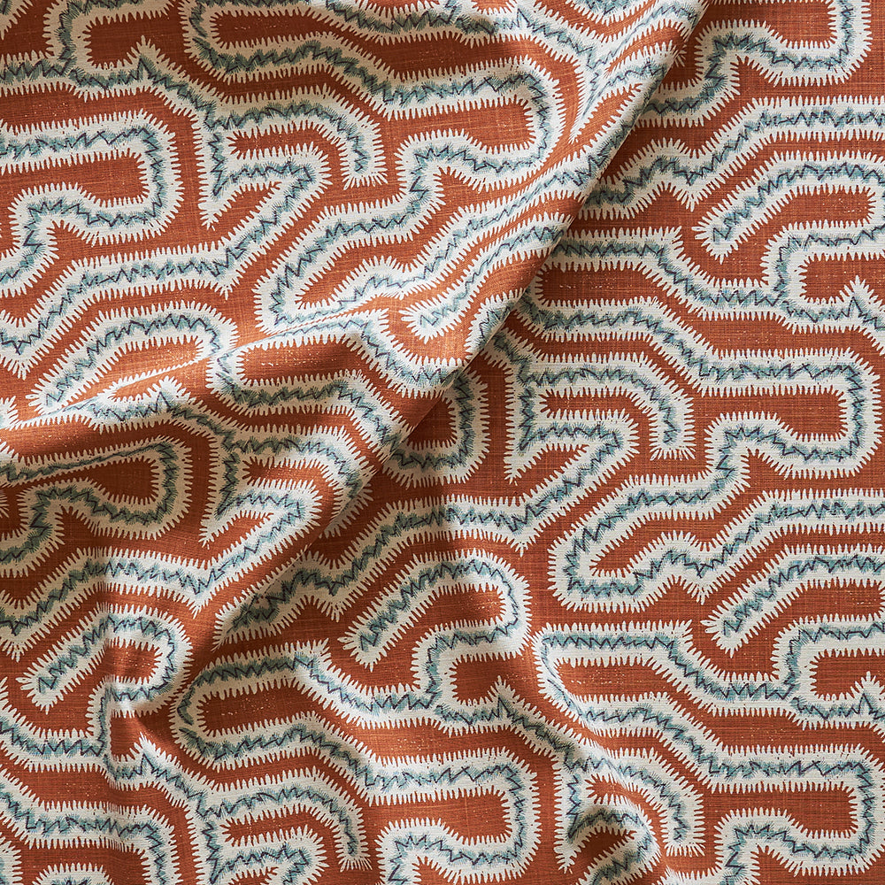 Draped fabric yardage in a dense meandering print in white, blue and gray on a burnt orange field.