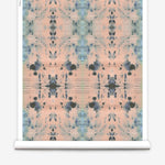 Partially unrolled wallpaper yardage in an abstract ink blot print in blue and gray on a light pink field.