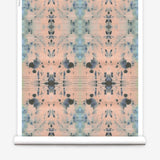 Partially unrolled wallpaper yardage in an abstract ink blot print in blue and gray on a light pink field.