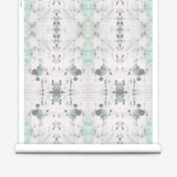 Partially unrolled wallpaper yardage in an abstract ink blot print in gray and green on a cream field.