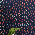 A vase of flowers stands in front of a wall covered in a playful paint blotch print in blue, pink and orange on a navy field.