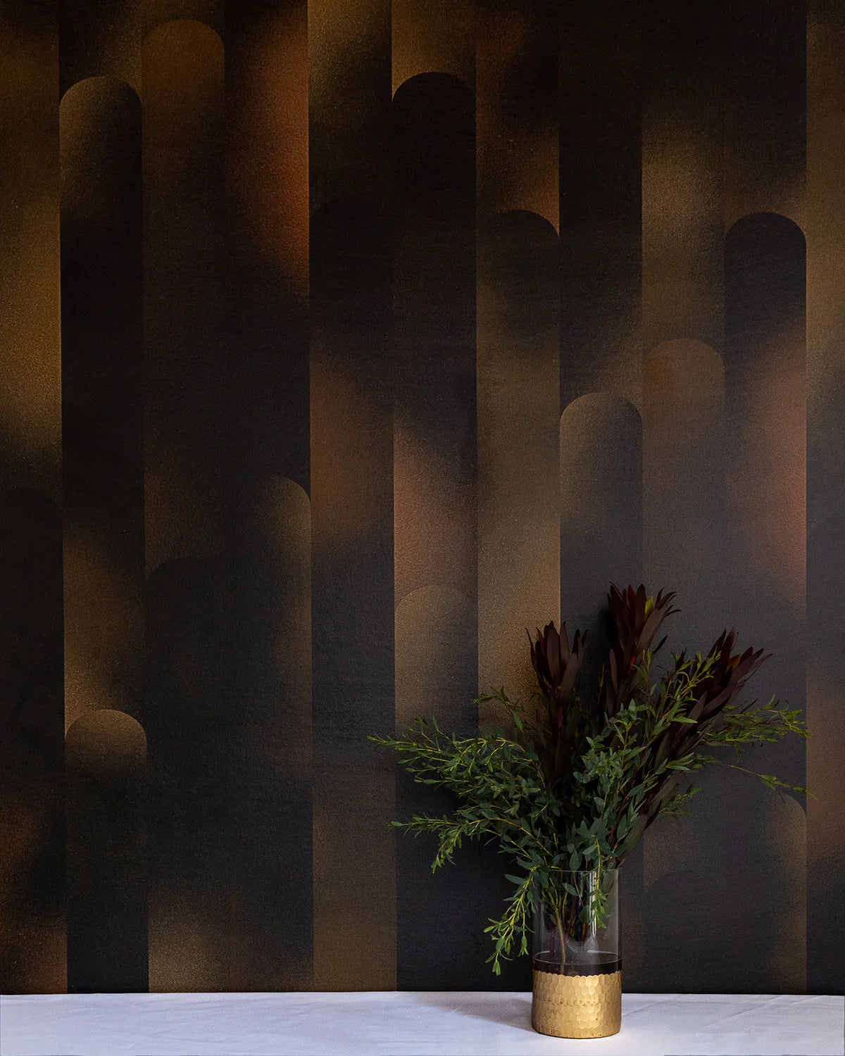 A vase of flowers stands in front of a wall covered in a curvilinear geometric print in shades of black and brown.