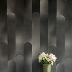 A vase of flowers stands in front of a wall covered in a curvilinear geometric print in shades of black and gray. 