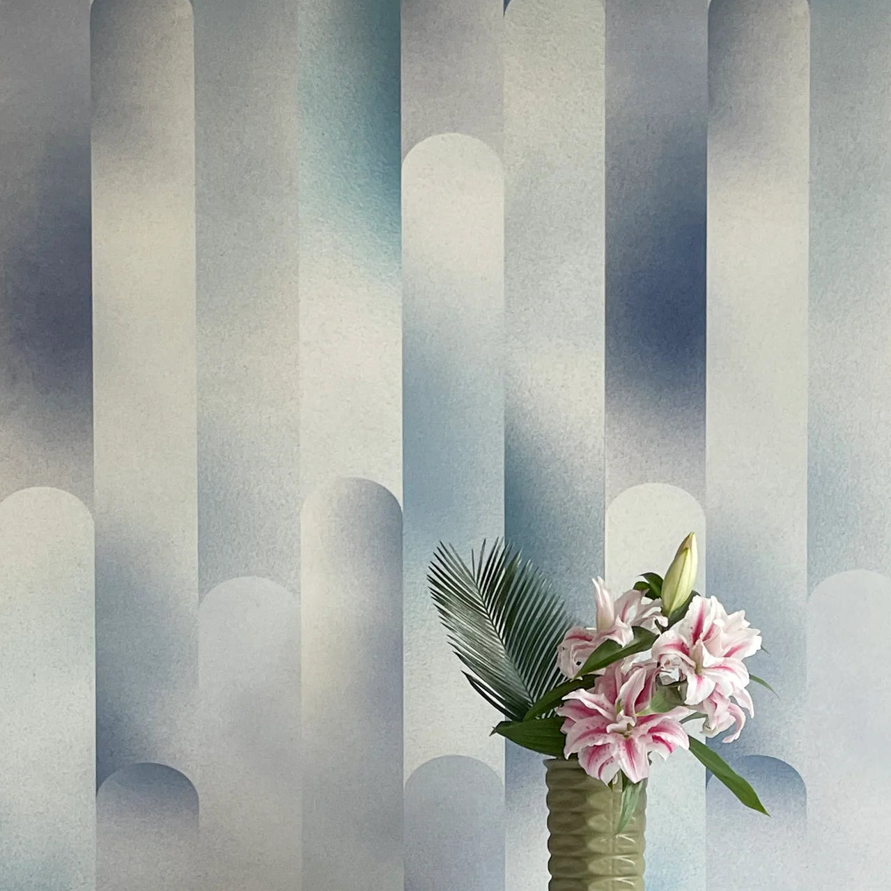 A vase of flowers stands in front of a wall covered in a curvilinear geometric print in shades of blue, turquoise and cream.