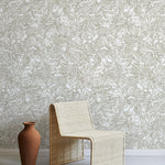 A straw chair and clay pot stand in front of a wall papered in a painterly wave print in white and tan.