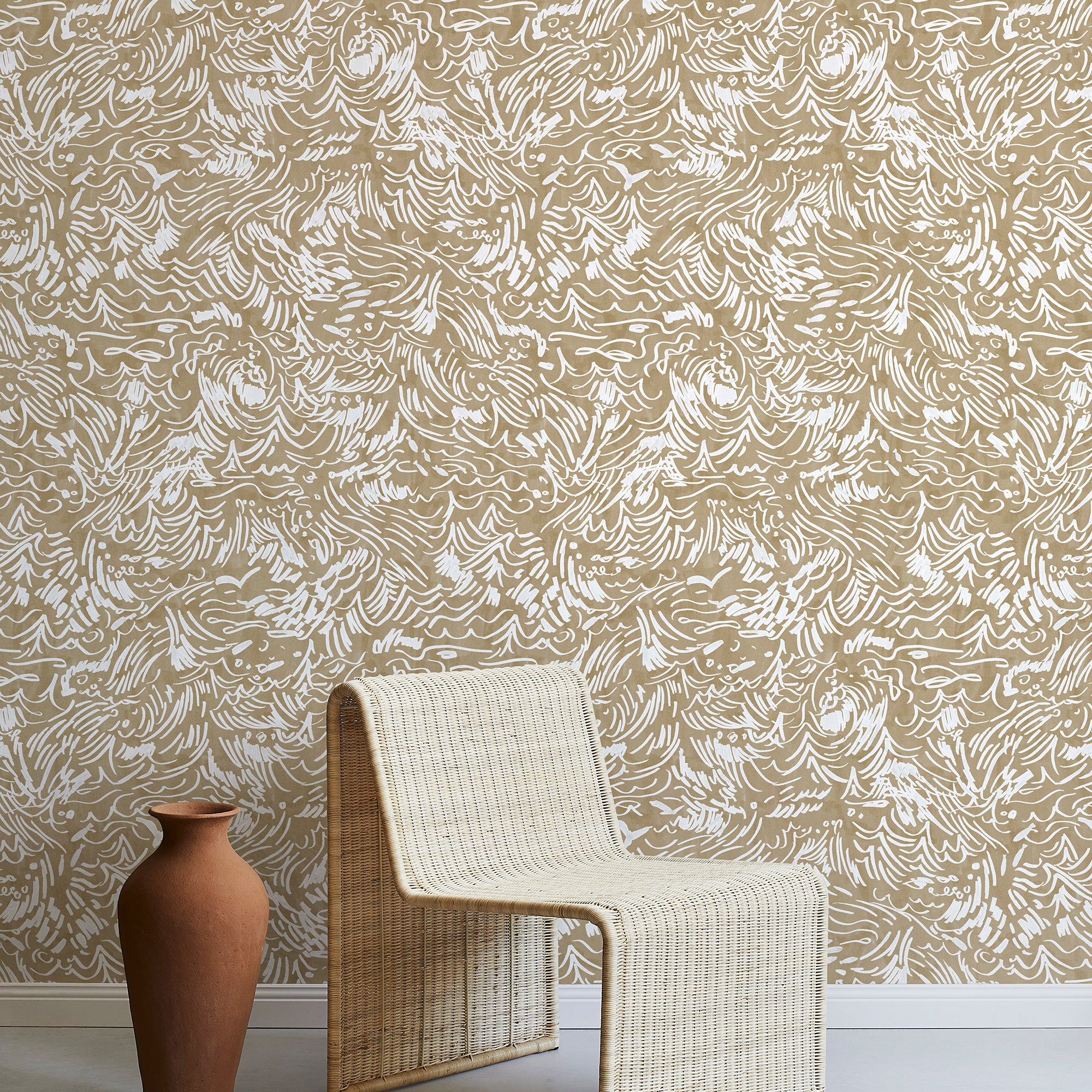 A straw chair and clay pot stand in front of a wall papered in a painterly wave print in white and light brown.