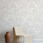 A straw chair and clay pot stand in front of a wall papered in a painterly wave print in white and cream.