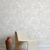 A straw chair and clay pot stand in front of a wall papered in a painterly wave print in white and cream.