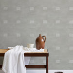 A bench with a towel and clay vases stands in front of a wall papered in a gridded dash print in white and sage.