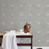 A bench with a towel and clay vases stands in front of a wall papered in a gridded dash print in white and sage.