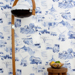 A lamp and end table stand in front of a wall papered in a playful illustrated city print in navy, blue and white.