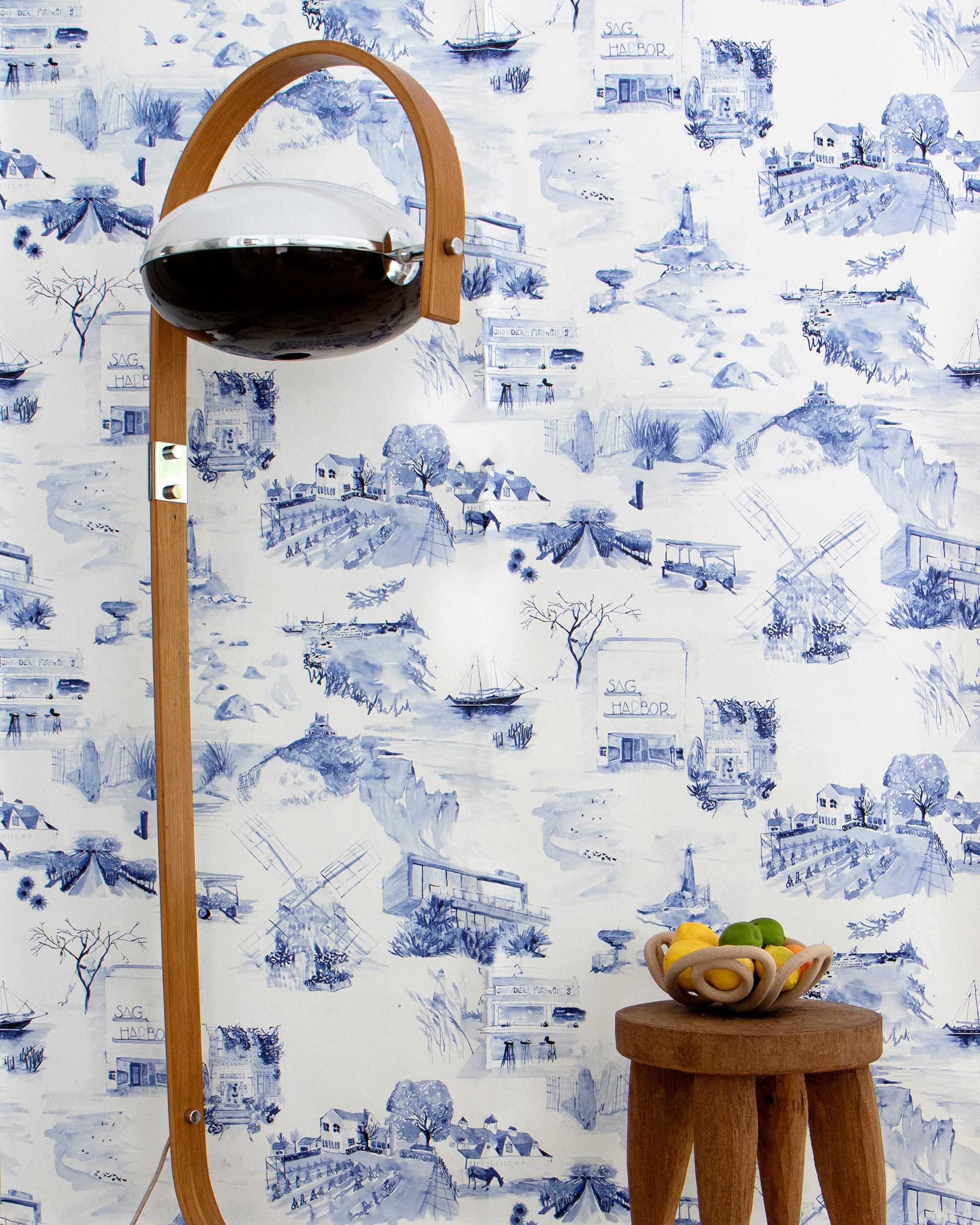 A lamp and end table stand in front of a wall papered in a playful illustrated city print in navy, blue and white.