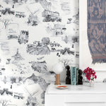 A cluttered sideboard stands in front of a wall papered in a playful illustrated city print in gray, black and white.