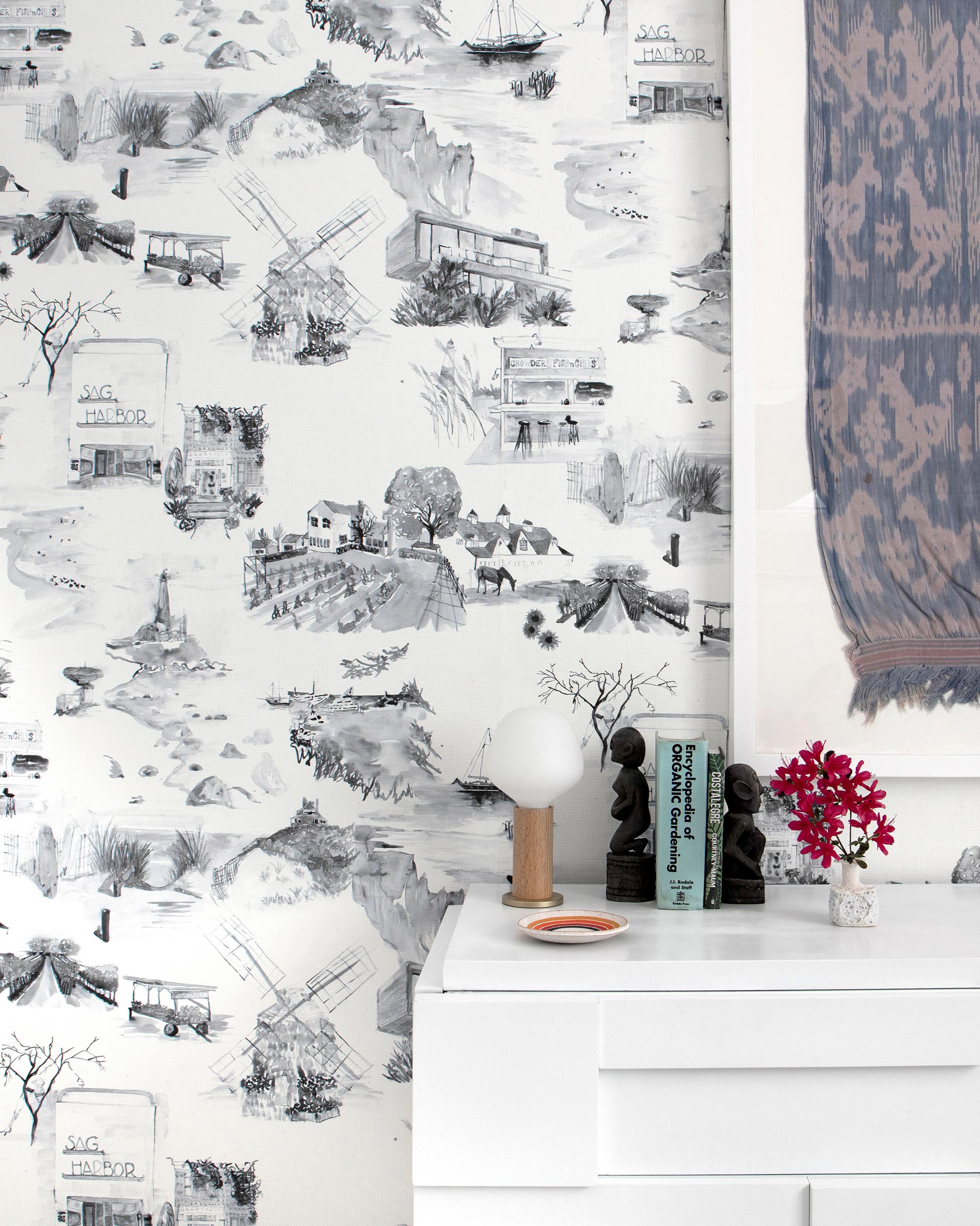 A cluttered sideboard stands in front of a wall papered in a playful illustrated city print in gray, black and white.