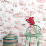 A chair, flowers and a basket stand in front of a wall papered in a playful illustrated city print in pink, brown and white.