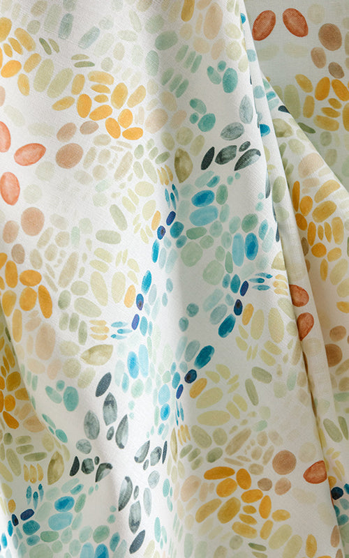 Draped fabric yardage in a painterly grid print in shades of blue, gray, and orange on a cream field.