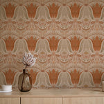 A table with a vase and cups stands in front of a wall papered in a floral damask print in coral, gray and cream.