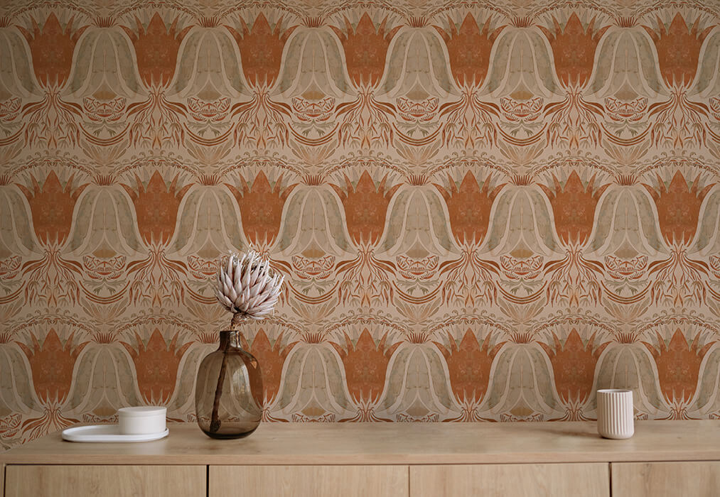 A table with a vase and cups stands in front of a wall papered in a floral damask print in coral, gray and cream.