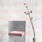 A modernist chair and plant stand in front of a wall papered in a painterly palm tree stripe print in pink, gray and white.