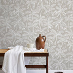 A bench with a towel and clay vases stands in front of a wall papered in a palm tree and monkey print in white and gray.