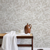 A bench with a towel and clay vases stands in front of a wall papered in a palm tree and monkey print in white and gray.