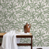 A bench with a towel and clay vases stands in front of a wall papered in a palm tree and monkey print in green and cream.