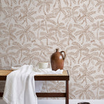 A bench with a towel and clay vases stands in front of a wall papered in a palm tree and monkey print in tan and cream.