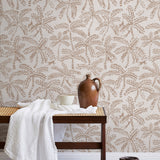 A bench with a towel and clay vases stands in front of a wall papered in a palm tree and monkey print in tan and cream.