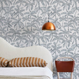 A modernist bed, hanging lamp and chair stand in front of a wall papered in a palm tree and monkey print in gray and white.