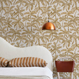 A modernist bed, hanging lamp and chair stand in front of a wall papered in a palm tree and monkey print in gold and cream.