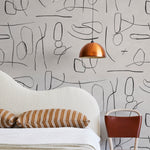 A modernist bed, hanging lamp and chair stand in front of a wall papered in an abstract shape pattern in black and tan.