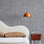 A modernist bed, hanging lamp and chair stand in front of a wall papered in an abstract shape pattern in white and gray.