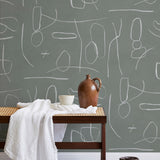 A bench with a towel and clay vases stands in front of a wall papered in an abstract shape pattern in white and sage.