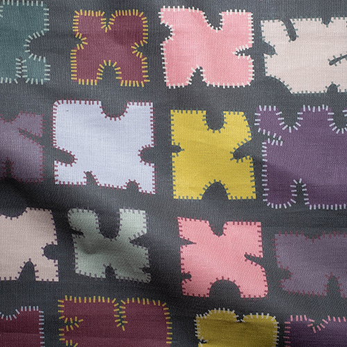 Draped fabric in a playful patchwork quilt print in a rainbow of shades on a dark green field.