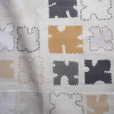 Draped fabric in a playful patchwork quilt print in neutral shades on a cream field.