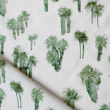 Draped fabric yardage in a painterly palm tree print in shades of green on a white field.