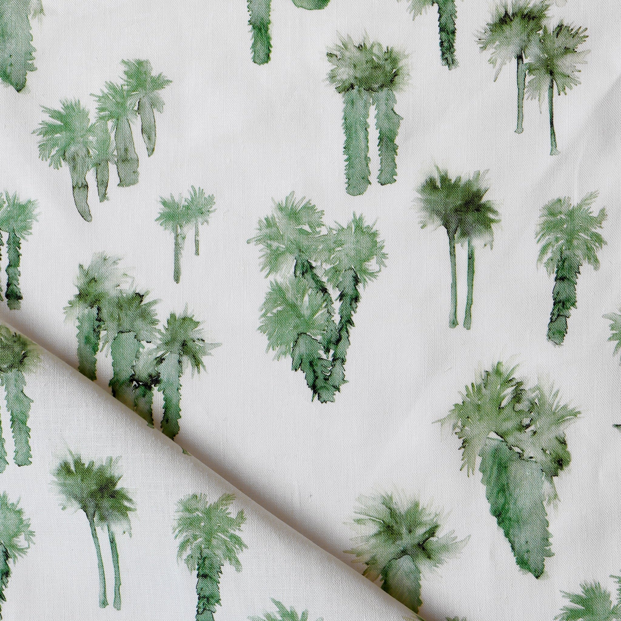 Draped fabric yardage in a painterly palm tree print in shades of green on a white field.